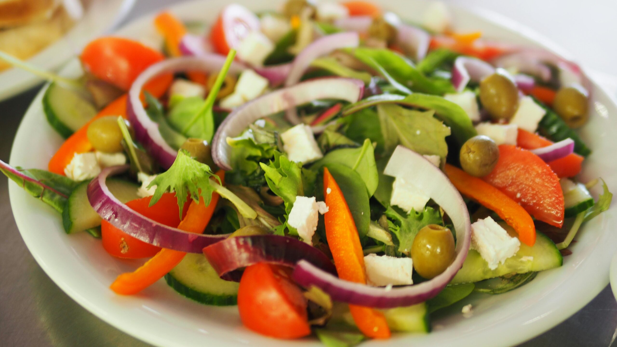 A plate of salad with fresh vegetables and crumbled feta cheese.