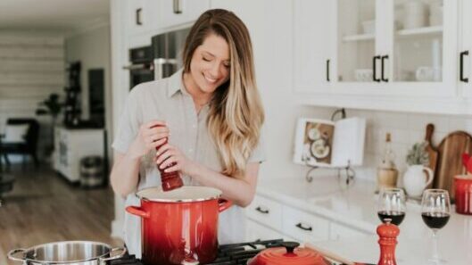 A woman cooking in a kitchen with red pots.