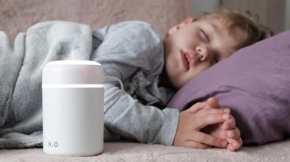 A child peacefully sleeping beside a white and pink humidifier, creating a soothing environment for better air quality.