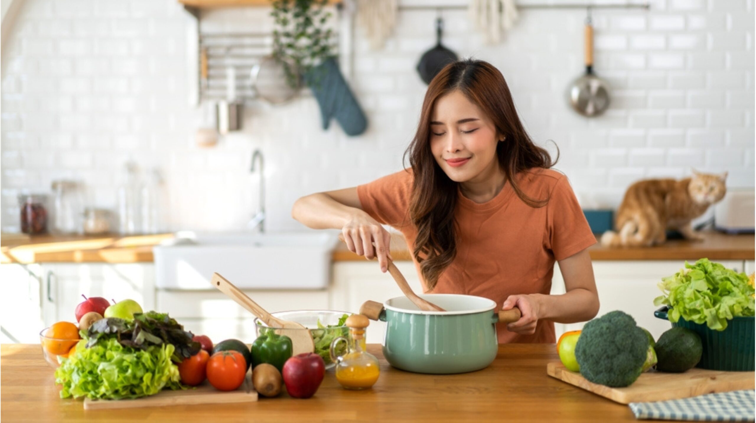 An Asian woman cooking a variety of vegetables in a modern kitchen.