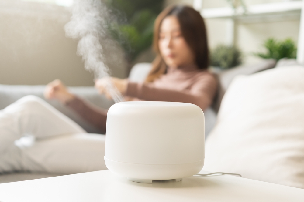 Woman sitting on couch in living room, using air humidifier. 