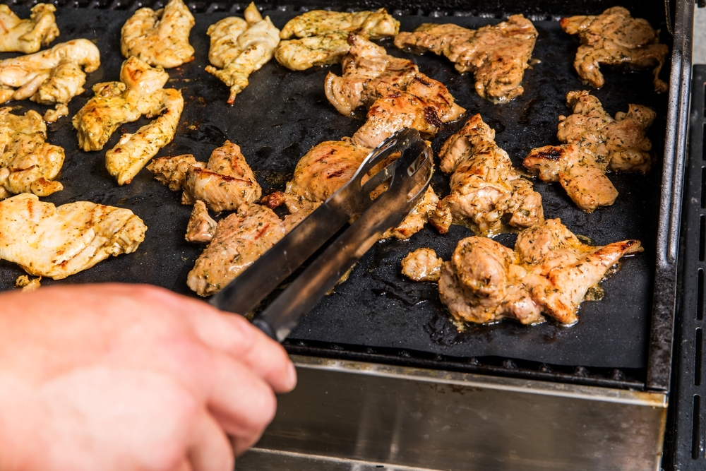 Chicken meats being stirred on non stick grill teflon mat. Grilled meat.