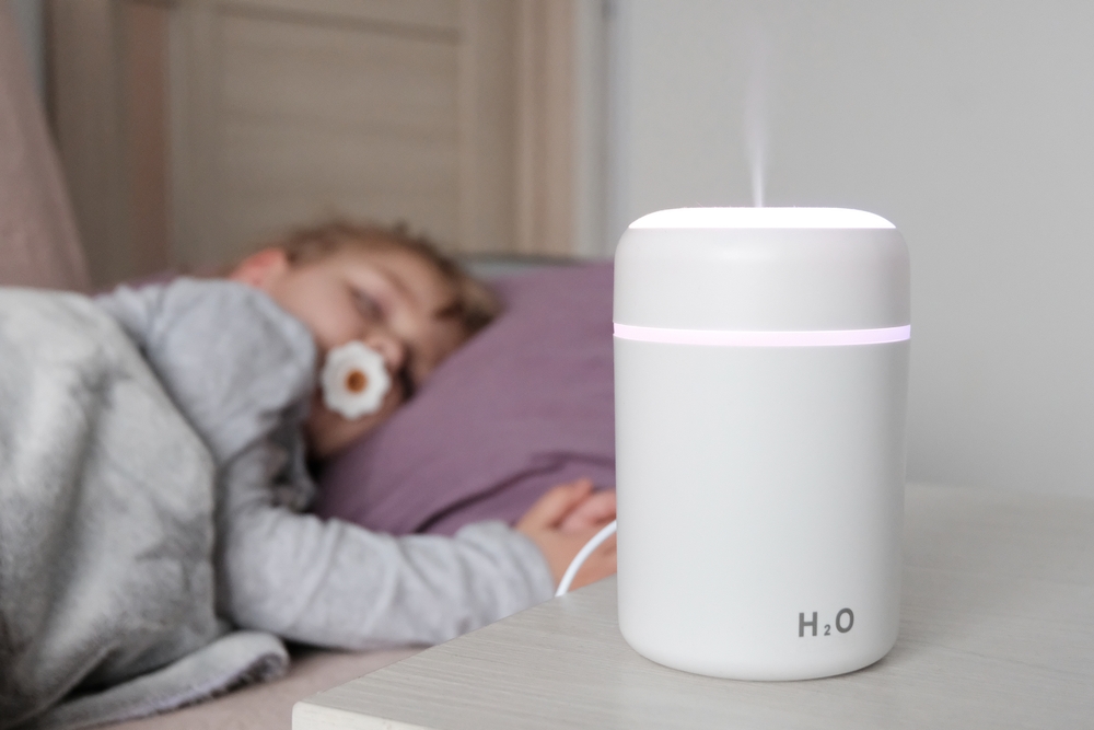 A sleeping child rests next to a humidifier, surrounded by a calming mist that promotes a restful sleep.