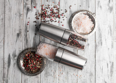 Electric spice mills. Made of metal. Nearby pepper and salt in metal cups. Gray wooden background. View from above.