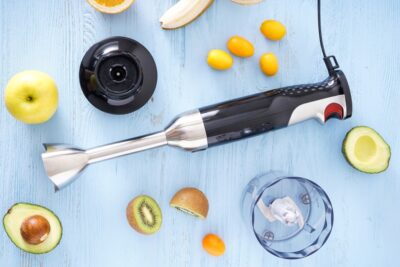 Hand blender and accessories with sliced fruit on a wooden background. Top view.