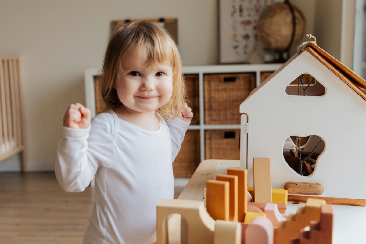 A child happily arranges wooden blocks to form a house, embodying the spirit of play and creativity in her surroundings