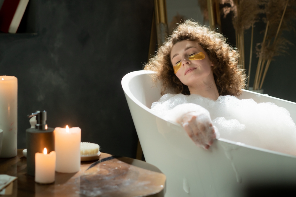 Pleasant caucasian woman puts on eye patches and relaxes in a bubble bath. The woman spends the evening relaxing in the bath and enjoying the aroma of scented candles.