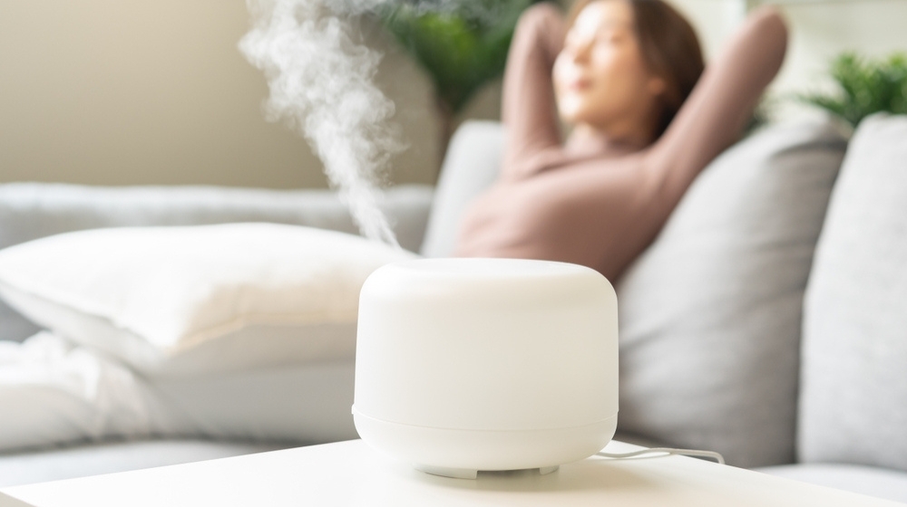 Modern air humidifier during relax or rest, happy blurred asian young woman, girl enjoying aromatherapy steam scent from essential oil diffuser comfortable in living conditions room,apartment at h