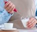 Woman in apron using a milk frother for making coffee at kitchen at home